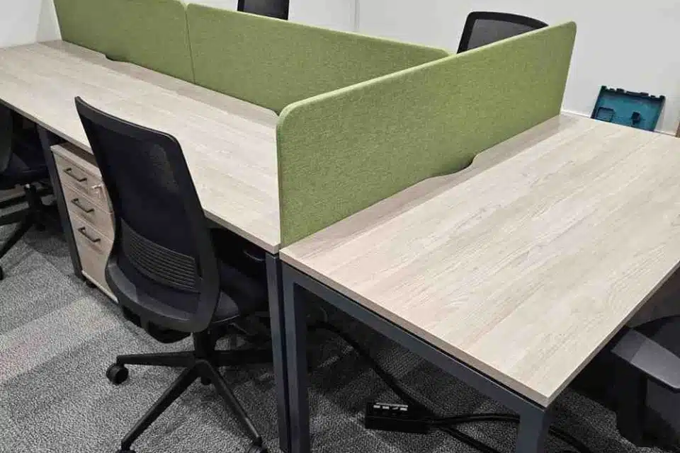 Modern office workstations arranged back-to-back, featuring light oak desks, lime green privacy