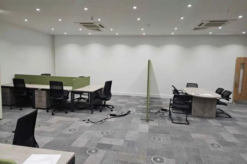 This open-plan office has modular workstations with green dividers, a matching meeting table, and built-in ceiling lights.