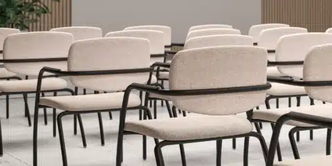 GAMA multi-purpose stackable office chair with black 4-leg frame and beige fabric upholstery in a conference room setting.