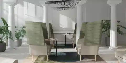 A bright office interior with white columns featuring high-back green and beige armchairs paired with slim black MOBI side tables on a decorative rug.