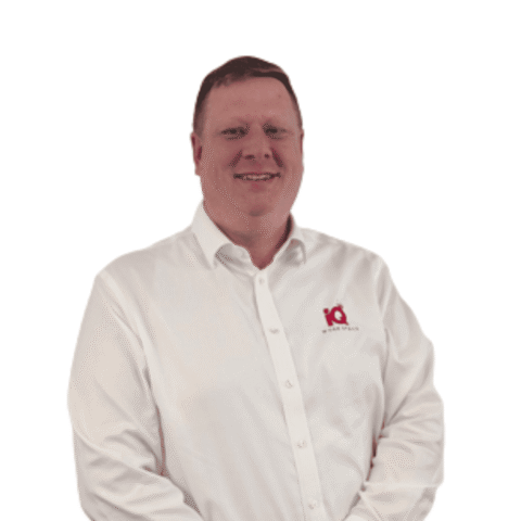 A white male smiling and standing in front of a white wall.