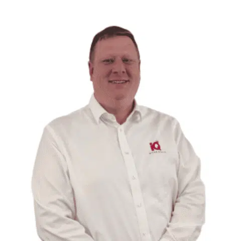 A white male smiling and standing in front of a white wall.