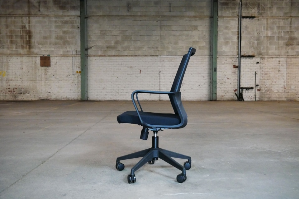 Side profile of a black Oslo mesh office chair showing the ergonomic curve of the backrest, integrated loop armrests, and the under-seat adjustment mechanisms.