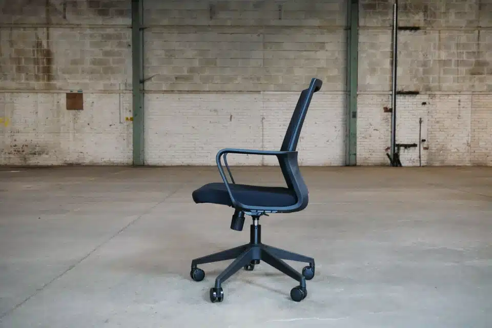 Side profile of a black Oslo mesh office chair showing the ergonomic curve of the backrest, integrated loop armrests, and the under-seat adjustment mechanisms.