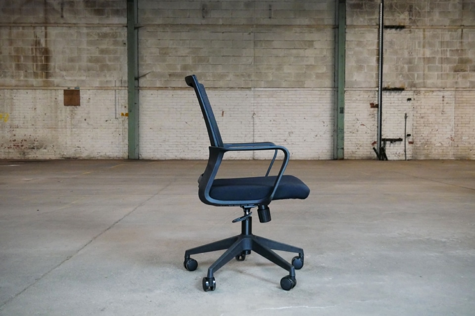 Side profile of a black Oslo mesh office chair showing the ergonomic curve of the backrest, integrated loop armrests, and the under-seat adjustment mechanisms.