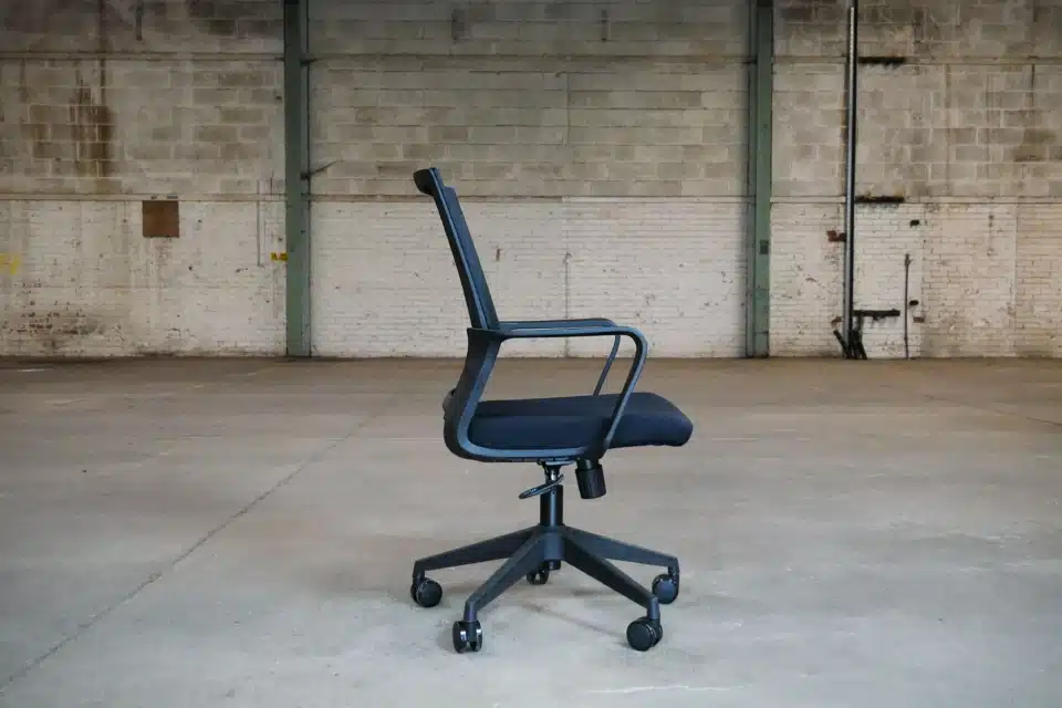 Side profile of a black Oslo mesh office chair showing the ergonomic curve of the backrest, integrated loop armrests, and the under-seat adjustment mechanisms.