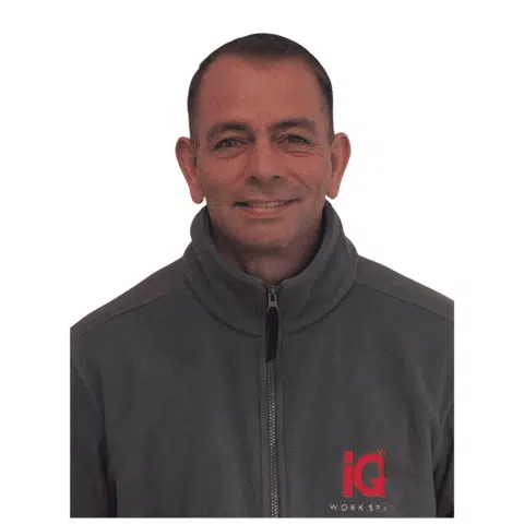 A white male smiling and standing in front of a white wall.