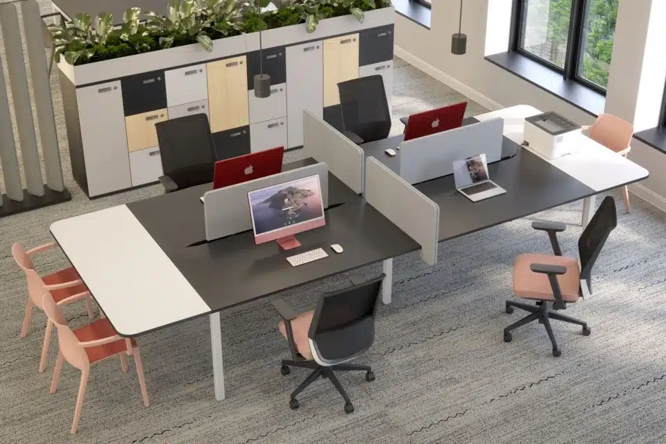 An overhead view shows a modern co-working space.Elite Loop task chairs have peach-colored upholstery and black frames.They sit at a shared workstation with gray privacy screens.