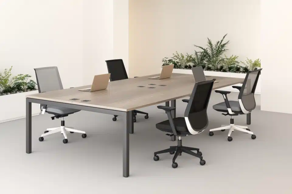 Four Elite Loop task chairs in a mix of grey and black finishes are arranged around a large light wood meeting table in a minimalist office setting.