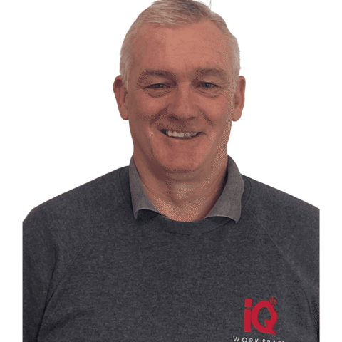 A white male smiling and standing infront of a white wall.