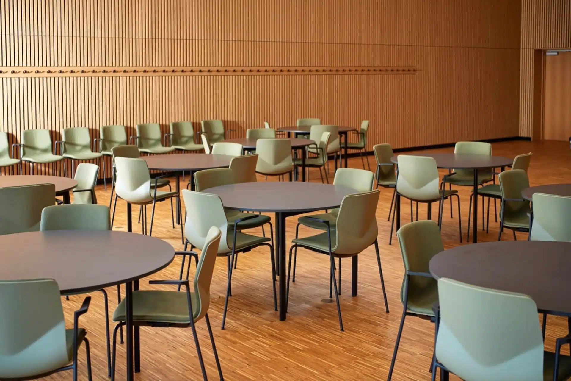 Modern, open-plan cafe or conference venue with sleek round tables and olive-green ergonomic chairs, ready for sustainable breakout sessions.