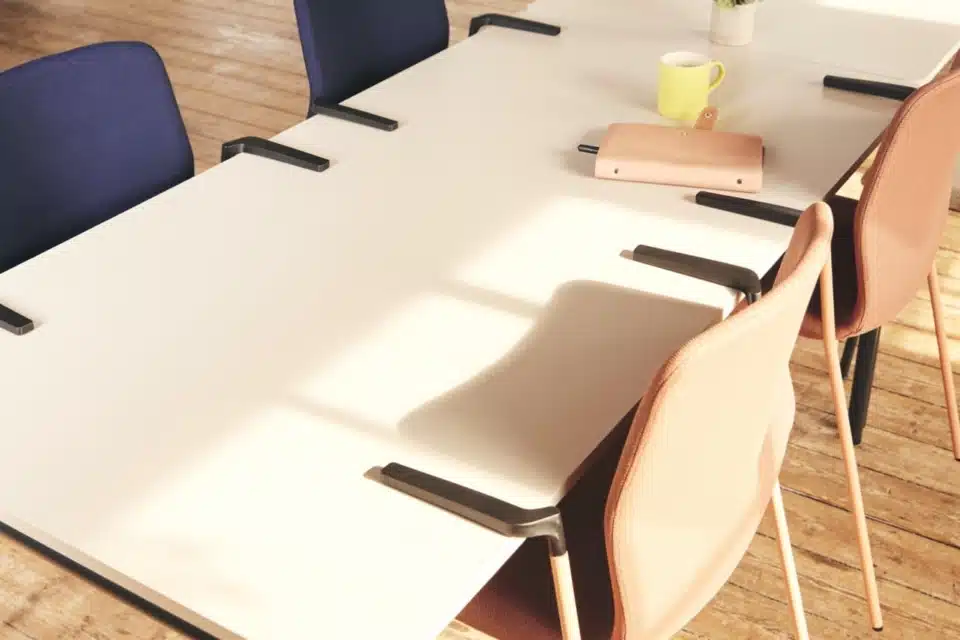 Fully upholstered FourSure 44 chairs in navy blue and terracotta pink suspended by integrated armrests from a white office table.