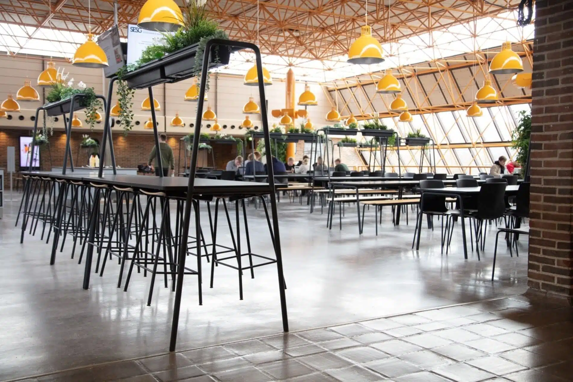 FourReal® 74 high tables with A-frame Room In Room planters in a large canteen.