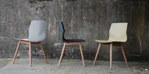 Three FourSure 44 chairs with wooden legs in white, black, and mustard yellow against a textured concrete wall.