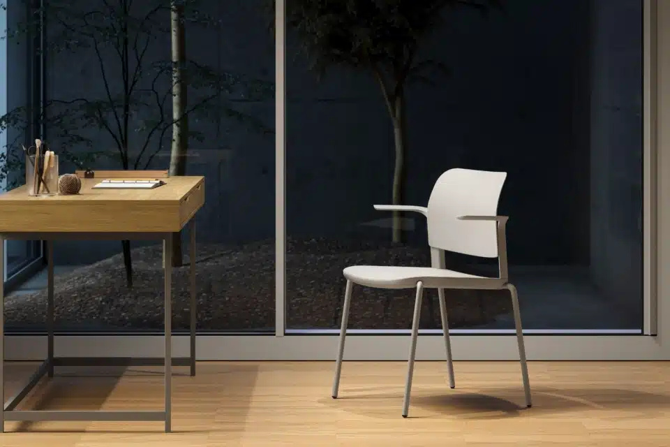 Modern iQ Workspace commercial office design featuring a compact light wood desk and an ergonomic light grey chair next to a large floor-to-ceiling window.