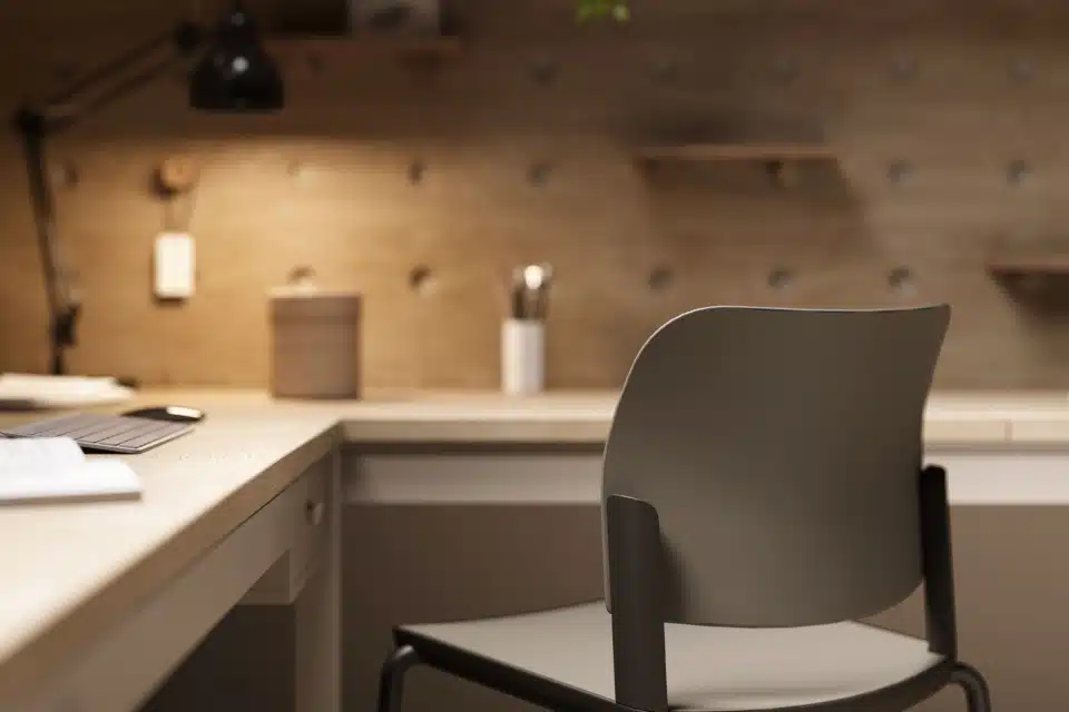 Close-up of a modern grey task chair at a light wood L-shaped desk with a wooden pegboard wall, highlighting warm commercial office design.