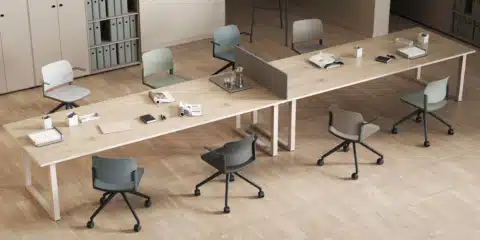 Modern commercial office design featuring a long wooden co-working desk with muted colour task chairs on a herringbone wooden floor.