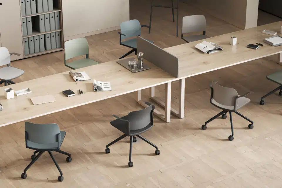 Modern commercial office design featuring a long wooden co-working desk with muted colour task chairs on a herringbone wooden floor.