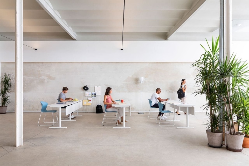Modern open-plan training room featuring individual white desks and light blue seating in a bright commercial office design.
