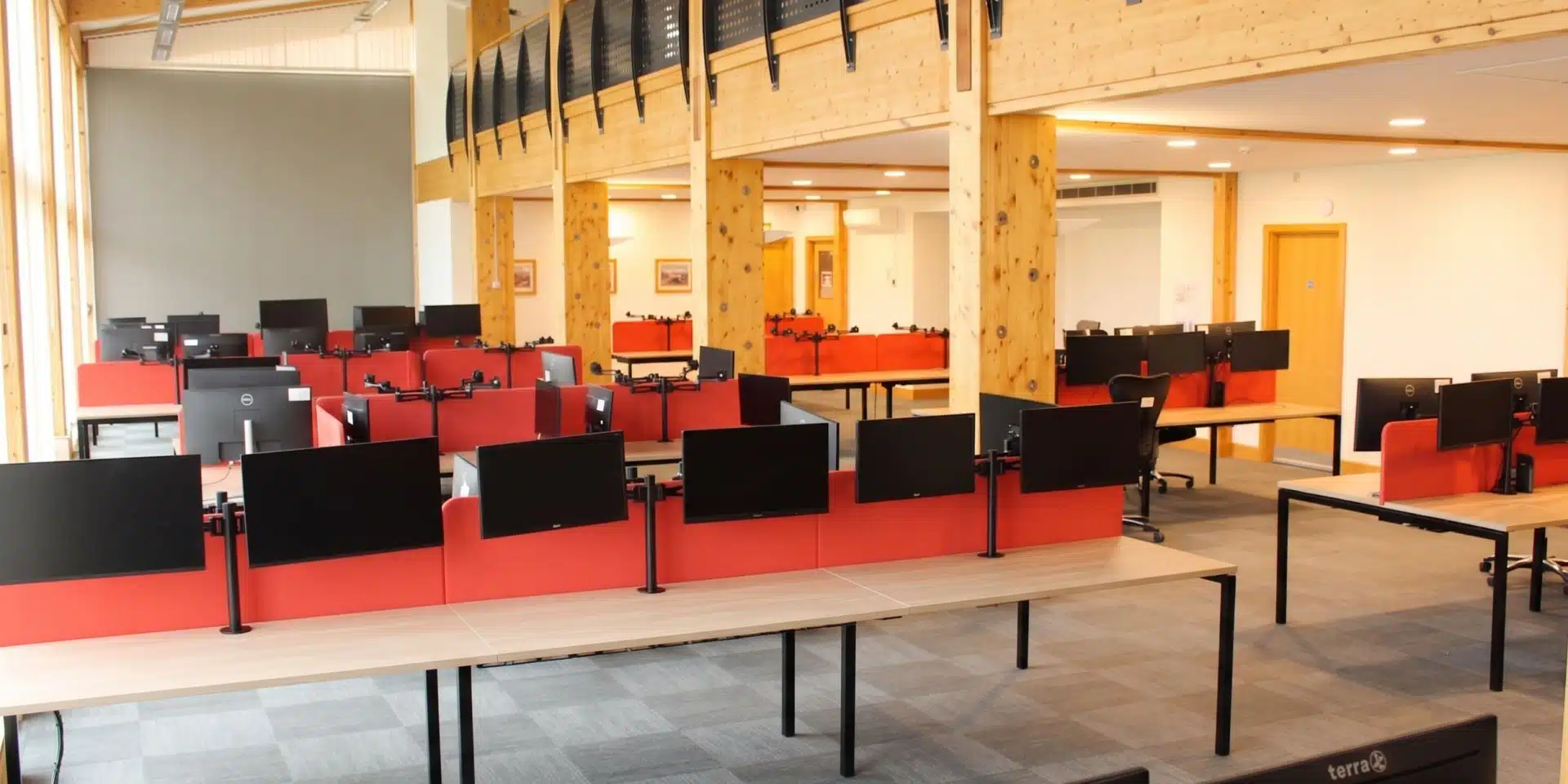 Bright open plan office space with wooden desks, red acoustic screens and dual monitor arms.