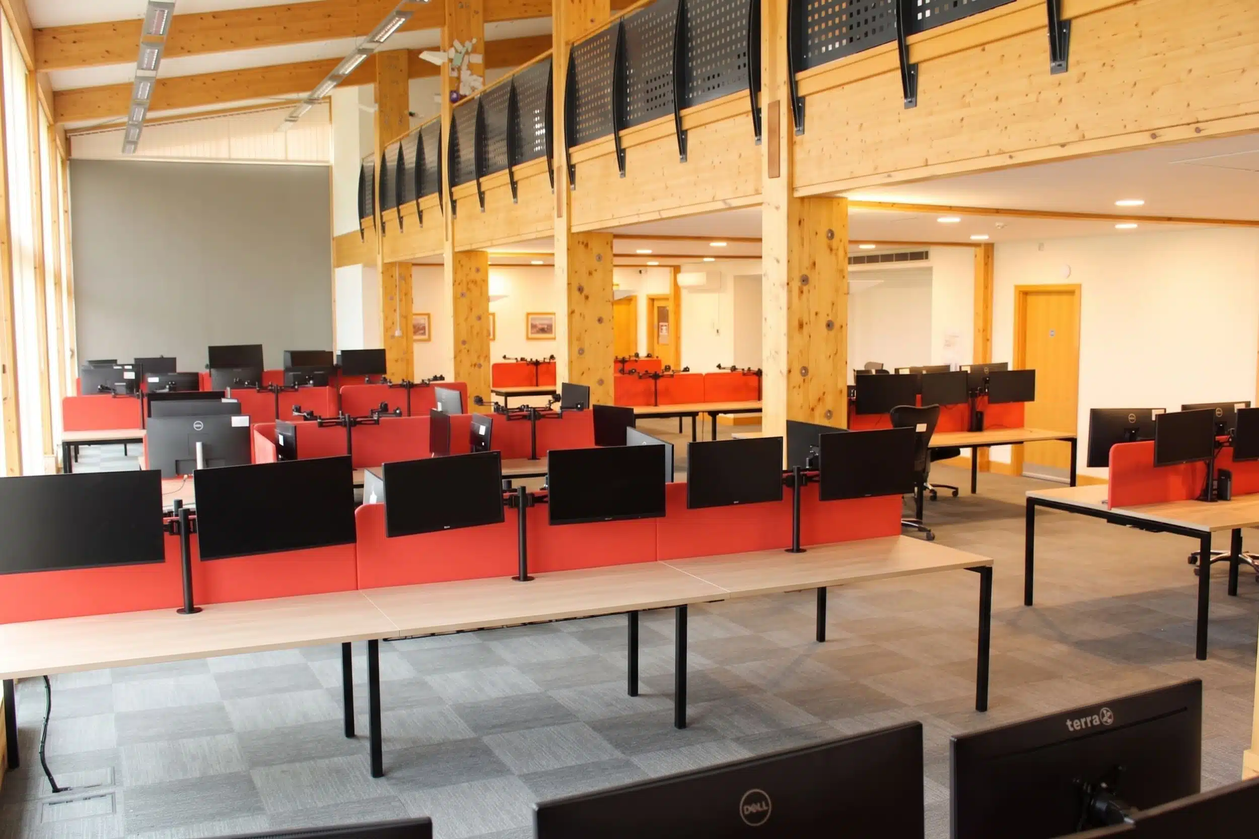 Bright open plan office space with wooden desks, red acoustic screens and dual monitor arms.
