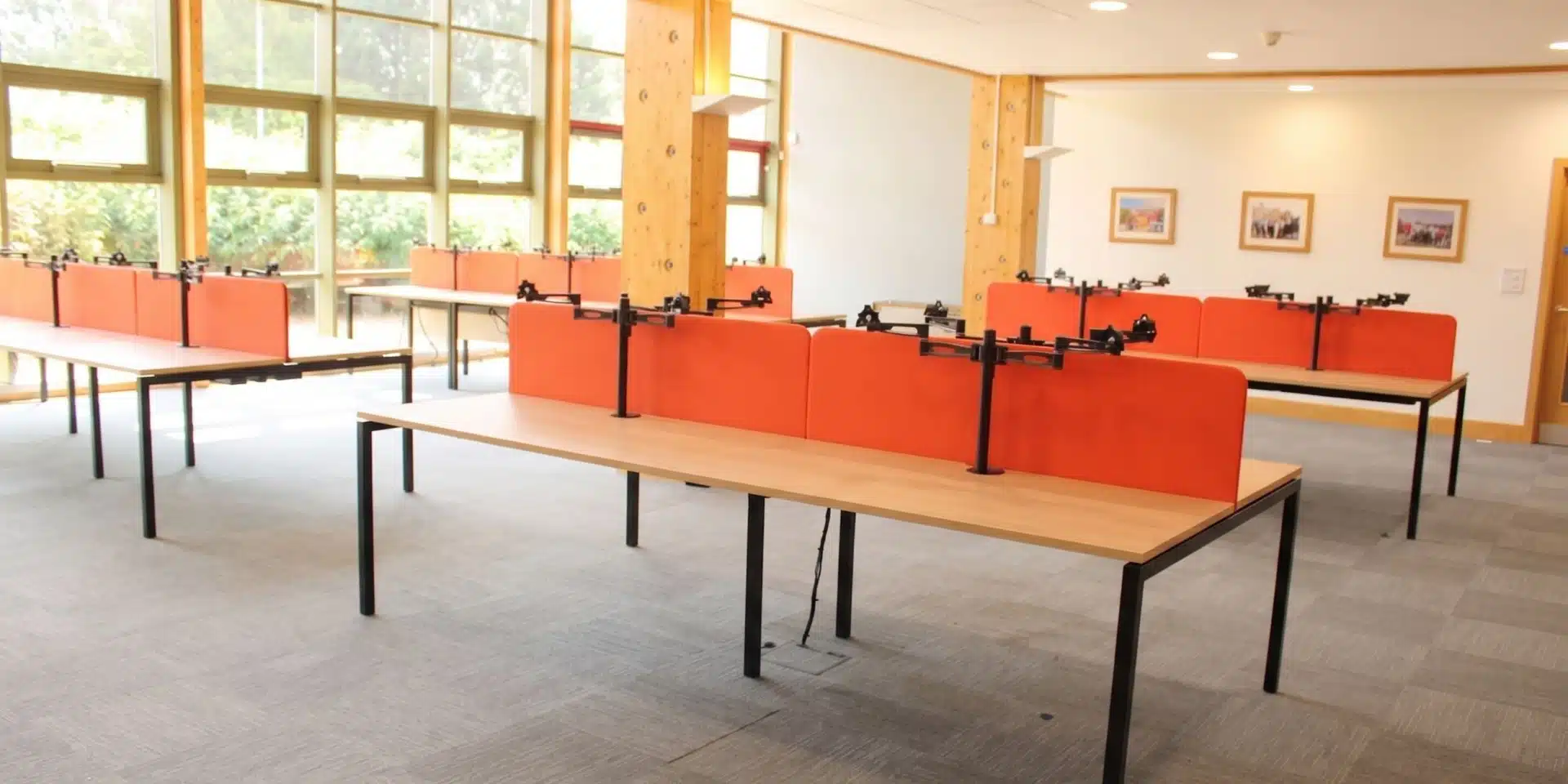 Sunlit office interior featuring modern workstations with red dividers and black monitor stands.