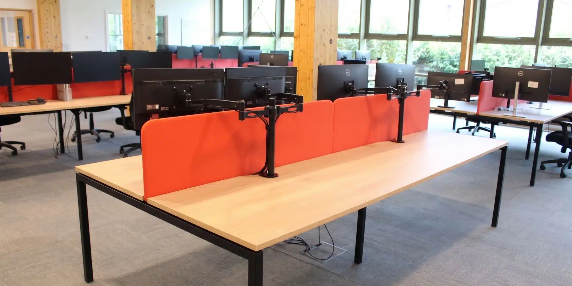 Sunlit office interior featuring modern workstations with red dividers and black monitor stands.