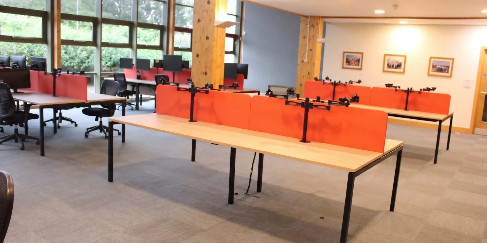 Modern commercial office furniture setup showing desks with red acoustic panels and large wooden pillars.