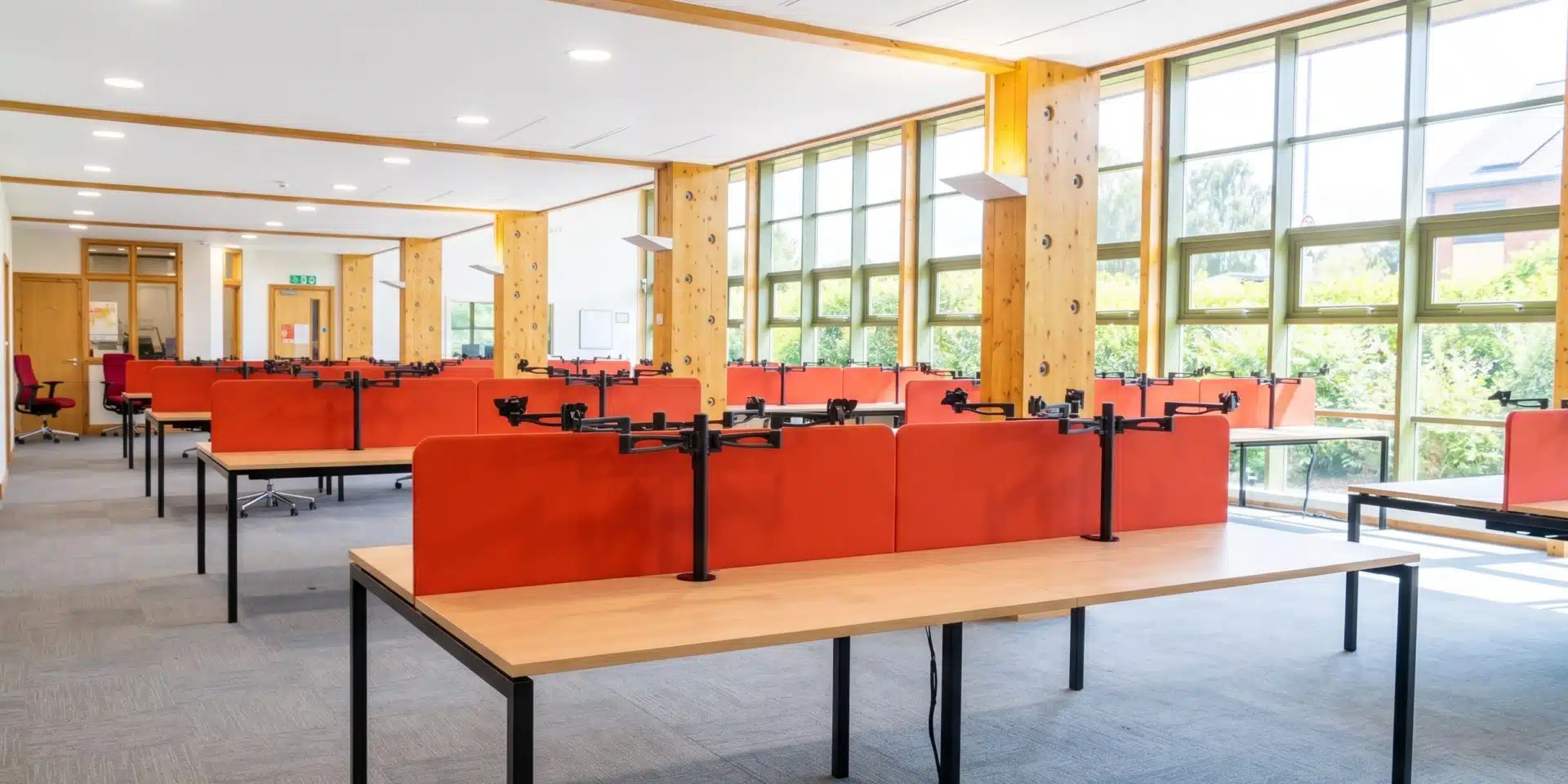 Modern commercial office furniture setup showing desks with red acoustic panels and large wooden pillars.
