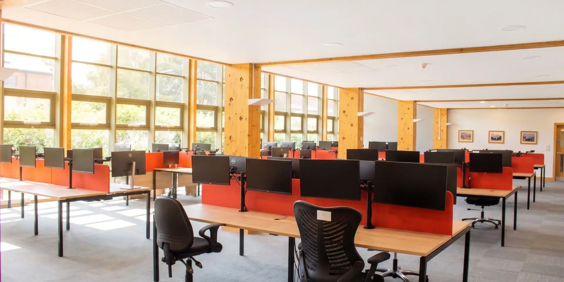 Bright open plan office space with wooden desks, red acoustic screens and dual monitor arms.