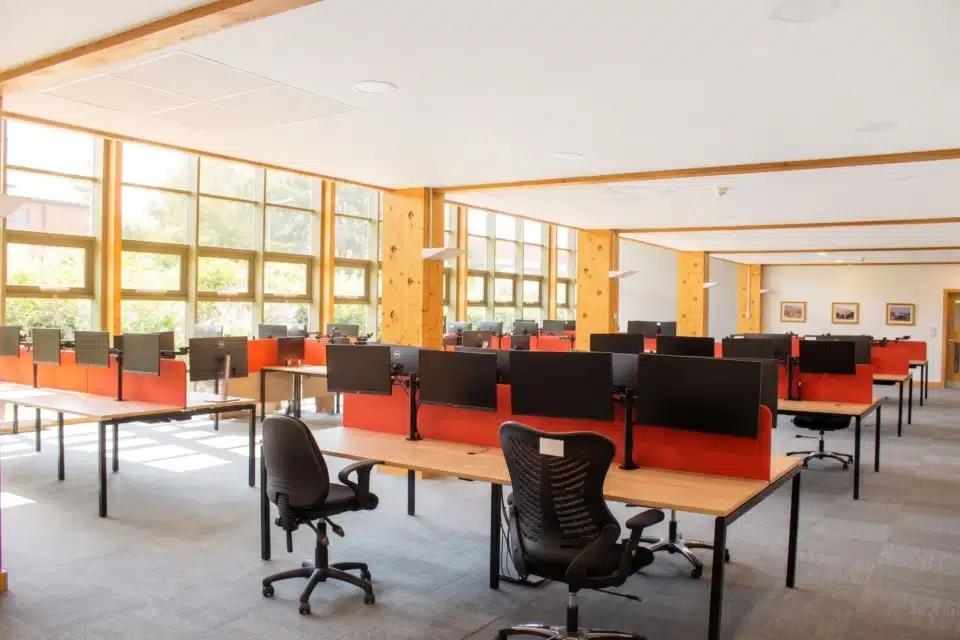 Bright open plan office space with wooden desks, red acoustic screens and dual monitor arms.